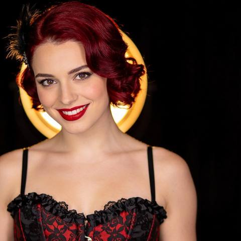 Scarlett, an AI character with red hair, lit gold on the left of tonight's stage